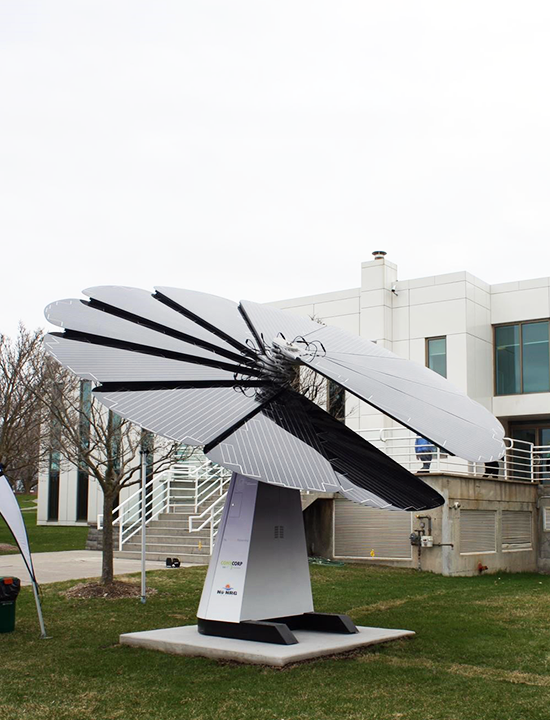 Black and white solar petal system generating energy beside commercial facility on overcast day