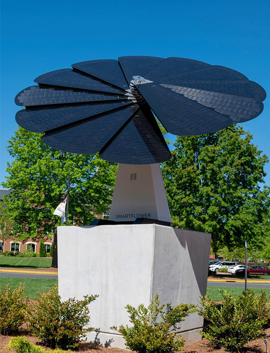 SmartFlower solar panel installation on raised concrete platform in a landscaped campus setting
