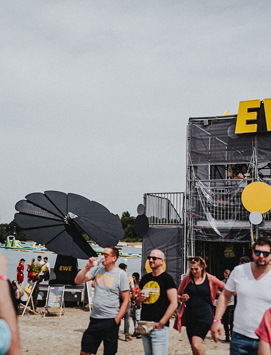 Crowd enjoying music festival powered by SmartFlower solar tech beside branded EWE structure