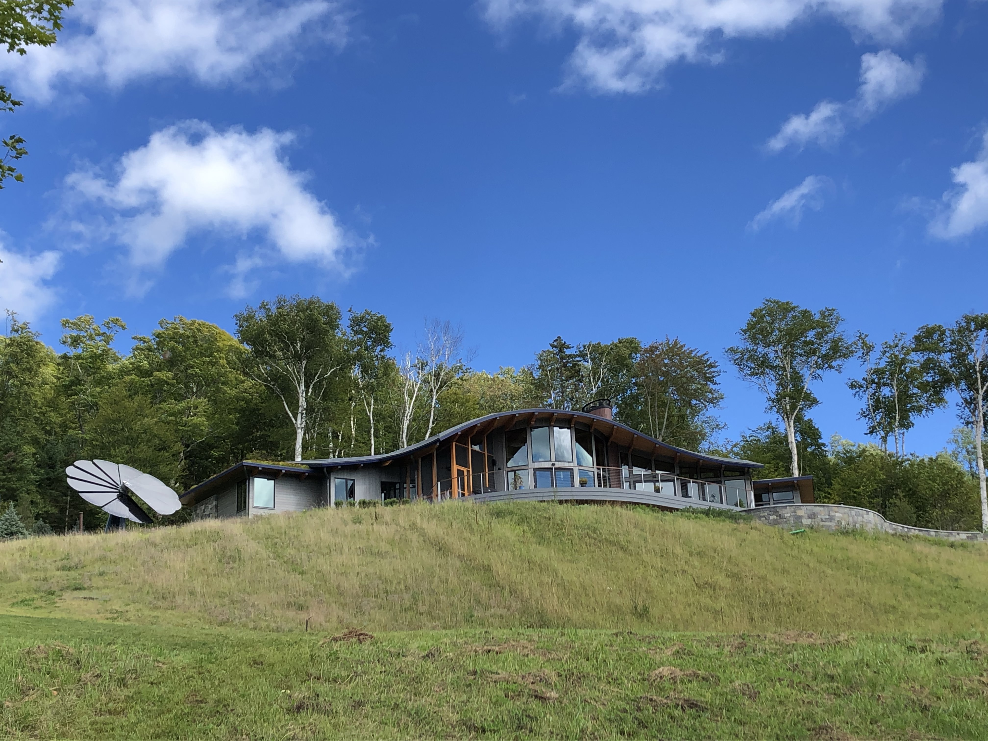 Modern hillside home with curved roof and SmartFlower solar panel set against lush forest backdrop