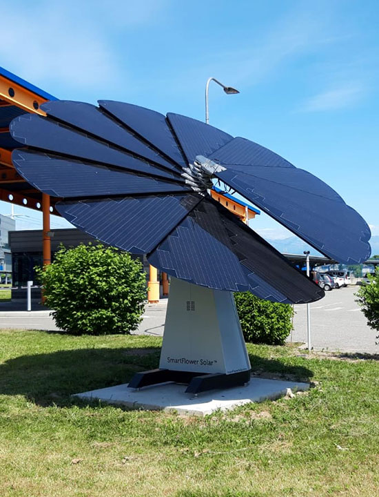 SmartFlower unit tilted toward sun near landscaped entrance to modern industrial complex
