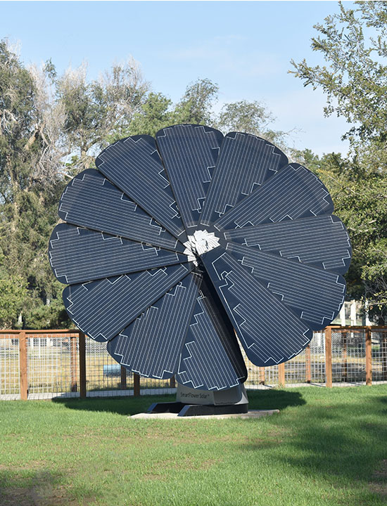 Standalone SmartFlower generating solar power in landscaped yard with wire and wood fencing