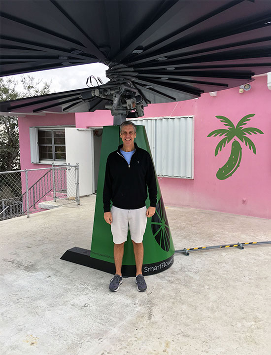 Person smiling under solar SmartFlower beside colorful building painted with palm tree and pickle