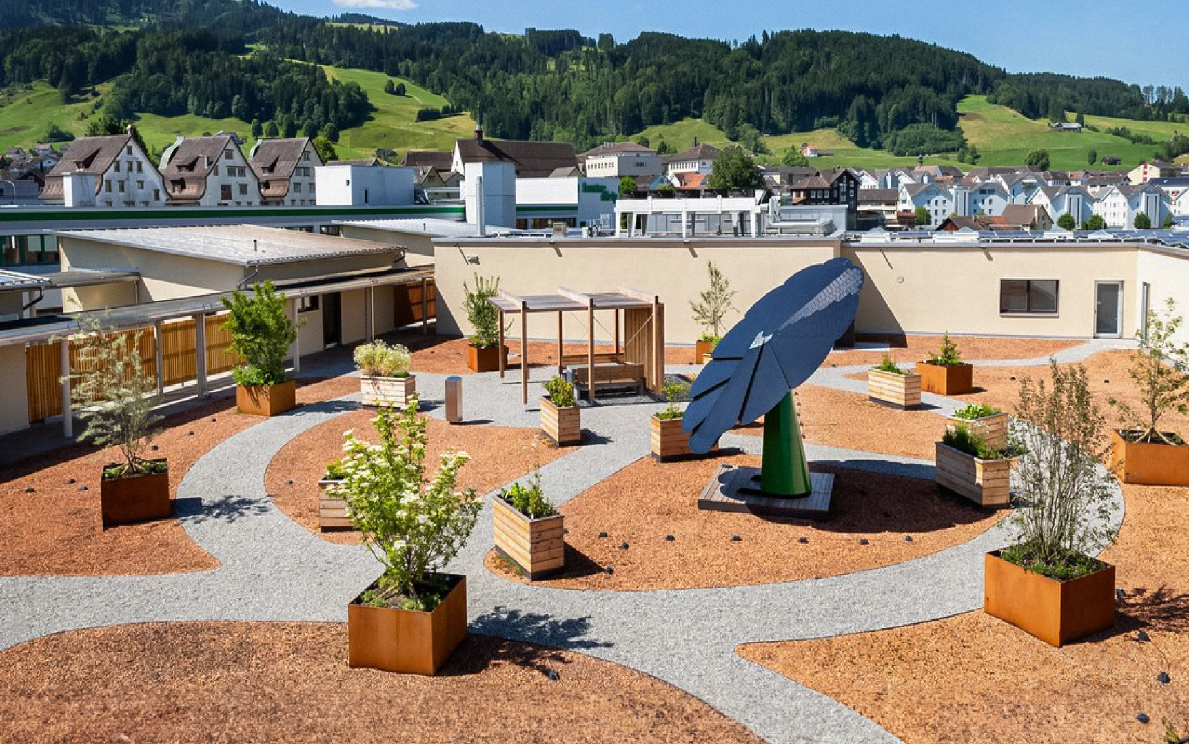 SmartFlower solar panel installed in rooftop garden with planter boxes and mountain village backdrop
