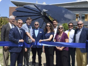 Community leaders celebrate sustainable energy launch with blue ribbon in front of SmartFlower installation