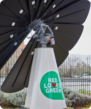 SmartFlower solar panel with “Red Loves Green” slogan promoting sustainability in landscaped urban area