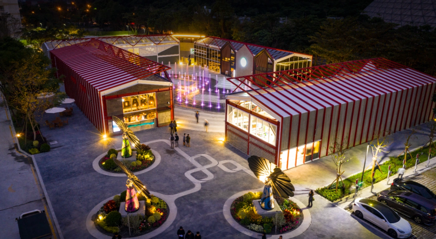 Night market plaza with colorful SmartFlower solar panels and striped-roof pavilions lit by spotlights