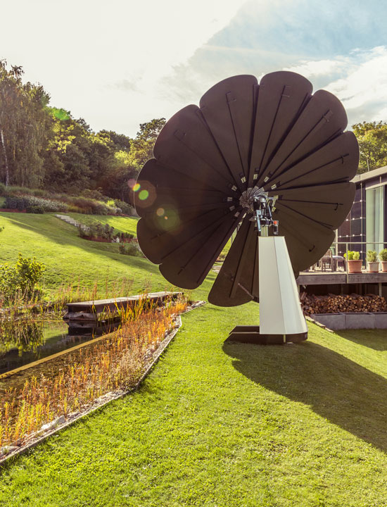 SmartFlower solar system facing sunlight on green lawn near landscaped garden and contemporary home
