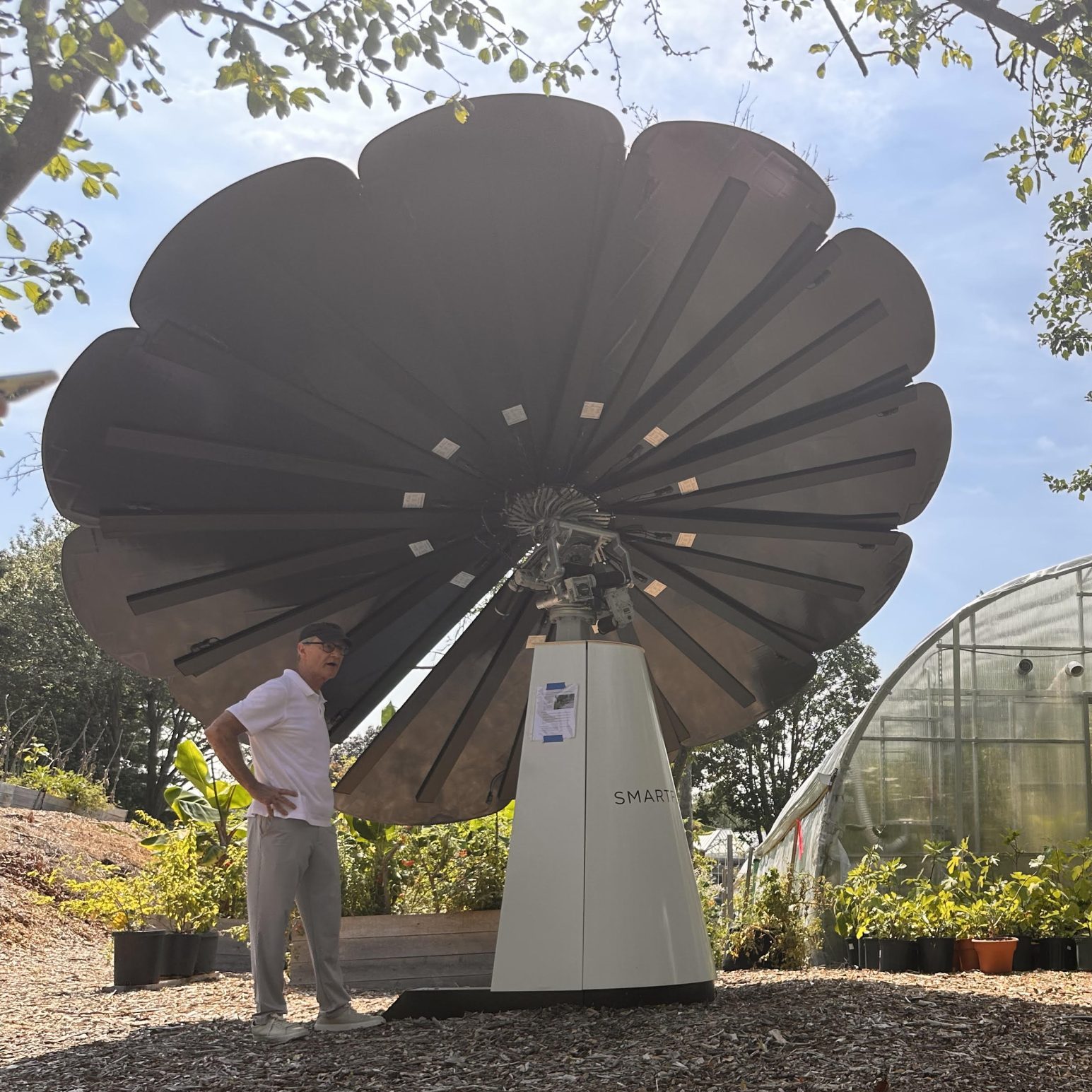 Man explains Smartflower solar technology to visitors during eco-friendly greenhouse garden demonstration