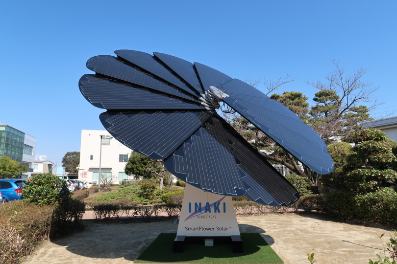 SmartFlower installed in a slab of concrete surrounded by landscaping with GomunoInaki's logo on the base of the unit.